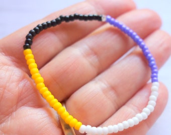 May include: A beaded bracelet with black, yellow, white and purple beads.