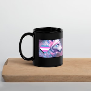 May include: Black ceramic mug with a white wolf design and a transgender pride heart on a black background.