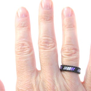 以下が含まれることがあります： 黒、紫、白のビーズでできたリングをつけた手