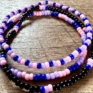 Può includere: Tre braccialetti a strati di perline in nero, rosa e viola.