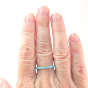 Op de afbeelding: Een hand met een dunne turquoise kralenring.