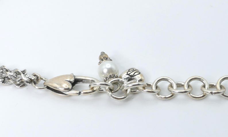 K&ouml;nnte beinhalten: Silberfarbene Halskette mit herzf&ouml;rmigem Verschluss und Perlenanh&auml;nger. Die Halskette hat auf einer Seite eine Doppel-Kette und auf der anderen Seite eine Reihe gro&szlig;er, runder Glieder. Ein kleiner Anh&auml;nger mit Perle und Zierelement ist ebenfalls vorhanden.