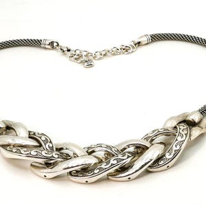 May include: Silver-toned necklace featuring a braided chain design. The necklace has a woven chain and a series of large, textured links with etched detailing. The clasp is a small lobster claw style.