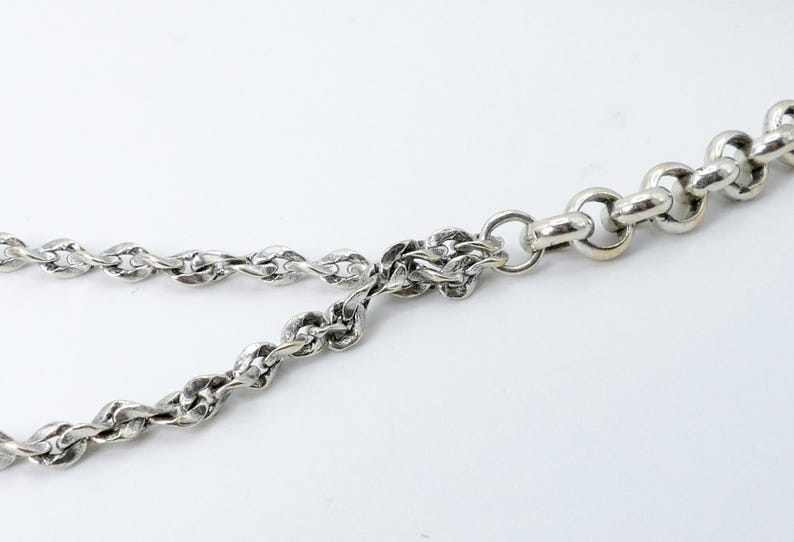 K&ouml;nnte beinhalten: Nahaufnahme einer silberfarbenen Halskette mit verschiedenen Gliedermustern. Die Kette wird vor einem wei&szlig;en Hintergrund pr&auml;sentiert, der die komplizierten Details der Metallarbeiten hervorhebt. Die Halskette ist ein Schmuckst&uuml;ck.