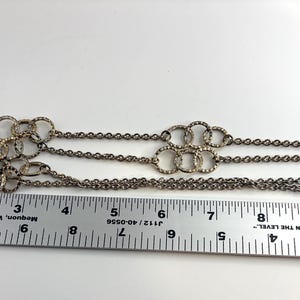 Puede incluir: Collar plateado con cadena y m&uacute;ltiples conjuntos de c&iacute;rculos entrelazados. El collar mide aproximadamente 28 cm de largo, medido con una regla.