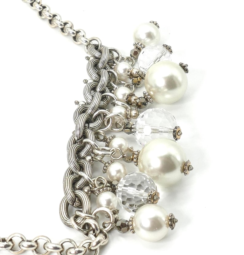 K&ouml;nnte beinhalten: Silberfarbene Halskette mit einer klobigen Kette und einer Kaskade aus Kunstperlen und facettierten, klaren Perlen. Die Halskette hat gro&szlig;e und kleine Perlen mit dekorativen Metallakzenten. Ein stilvolles Accessoire.