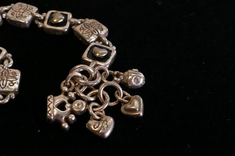 May include: Silver-toned charm bracelet with square links and various charms. Charms include hearts, crowns, and a small bead with a clear stone. The bracelet has a vintage or antique aesthetic.