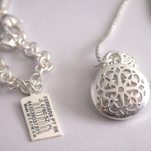 May include: A silver-toned necklace featuring a round pendant with an intricate cut-out filigree pattern. The chain includes a lobster clasp and a rectangular white tag printed with the text FERRARA PT NK JL4760 SZ PL 843036037975 Made in TAIWAN.