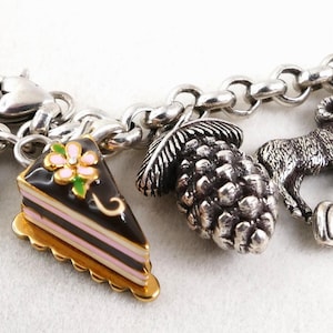May include: Silver charm bracelet with various charms. Charms include a Colorado flag, a slice of cake, a pinecone, a ram, and a Rocky Mountains charm. The charms are detailed and colorful, with enamel accents.
