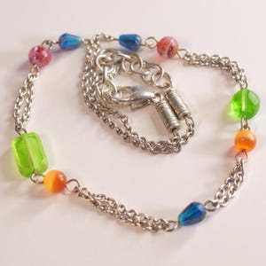 Puede incluir: Una pulsera de doble cadena en tono plateado con un surtido de cuentas de vidrio de colores. Las cuentas incluyen formas rectangulares de color verde transl&uacute;cido, esferas redondas naranjas y rosas, y cuentas azules en forma de l&aacute;grima, unidas por eslabones.