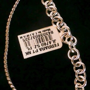 May include: A silver-toned necklace featuring a twisted chain segment and a series of circular links. A rectangular white tag is attached, displaying a barcode and the text: FERRARA PT NK, JL4760 SZ: PL, 843036037325, Made in TAIWAN.