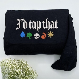 May include: Black sweatshirt featuring the phrase "I'd tap that" in white gothic lettering. Below are colourful symbols: a blue water drop, a green tree, a white skull, an orange flame, and a yellow sun. The sweatshirt is folded.