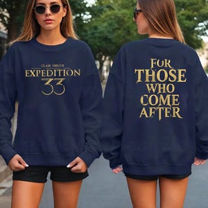 Puede incluir: Sudadera azul marino con texto dorado. En la parte delantera se lee "CLAIR OBSCUR EXPEDITION 33", y en la trasera "FOR THOSE WHO COME AFTER". Una prenda casual y cómoda.