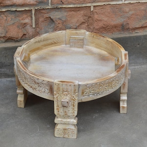 Peut inclure: Table ronde en bois blanc cassé avec des motifs floraux sculptés et quatre pieds robustes. La table a un bord surélevé et convient à l'affichage décoratif. La table mesure environ 30 cm de hauteur.