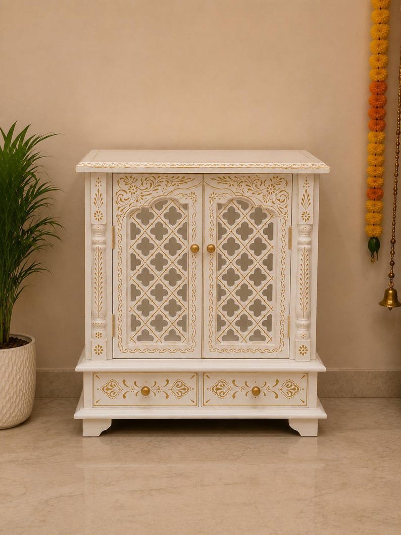 May include: A white wooden cabinet featuring two doors with intricate lattice cutouts and gold painted floral accents. The cabinet includes two lower drawers with gold knobs and decorative gold trim along the top and drawer fronts.