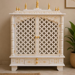 Op de afbeelding: Een witte houten kast met twee deuren in een latwerkpatroon, goudkleurige accenten en vijf gouden sierspitsen aan de bovenkant. De kast bevat een enkele lade met twee gouden knoppen, decoratieve bloemmotieven en vier stevige poten.