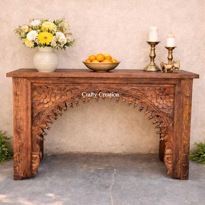 Può includere: Una consolle in legno intagliato con un motivo floreale, che contiene un vaso di fiori gialli e bianchi, una ciotola di arance e candelabri in ottone. Il tavolo ha il testo "Crafty Creation". Una ghirlanda di fiori gialli è appesa sopra.
