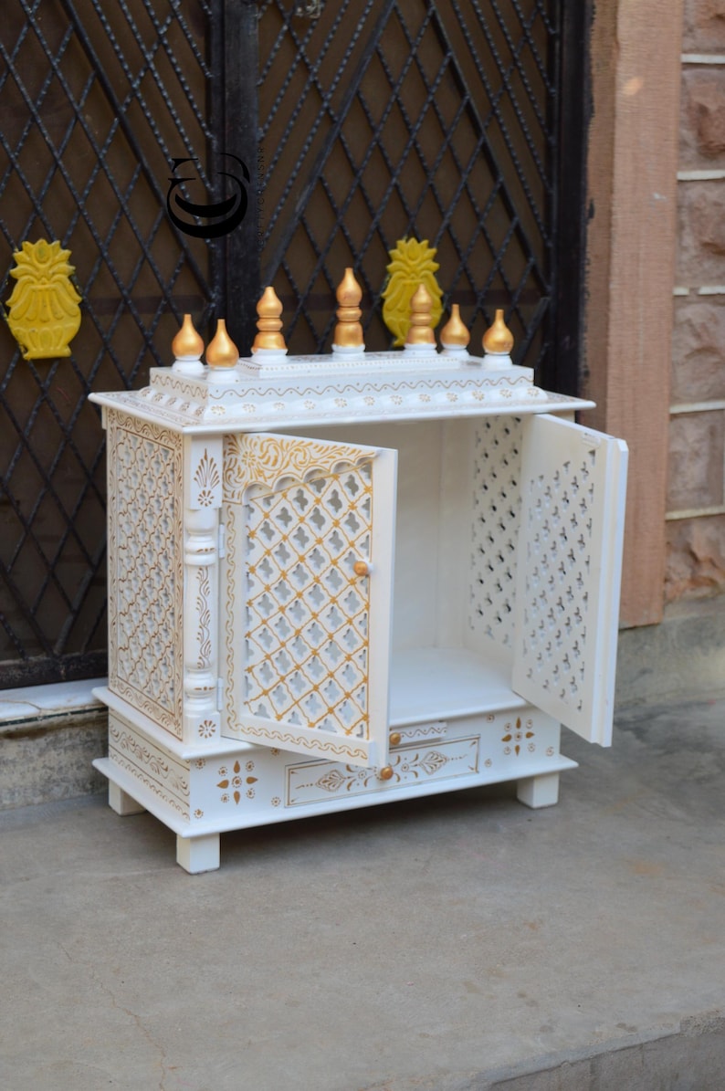 May include: A white wooden home temple cabinet featuring gold painted accents, intricate lattice work on the two open doors, and a small pull-out drawer at the base. The top is adorned with six gold finials and decorative carved patterns.