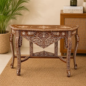 May include: A brown wooden console table with detailed white floral and geometric carvings. The table features a curved front, four curved legs, and an openwork design. The table is placed on a woven rug.