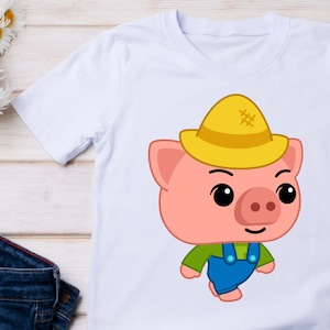 May include: White t-shirt featuring a cartoon pig wearing a yellow hat, green shirt, and blue overalls. The pig has a pink face, ears, and snout, with black eyes and a smile. The shirt is likely for children.