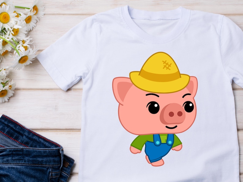 May include: White t-shirt featuring a cartoon pig wearing a yellow hat, green shirt, and blue overalls. The pig has a pink face, ears, and snout, with black eyes and a smile. The shirt is likely for children.