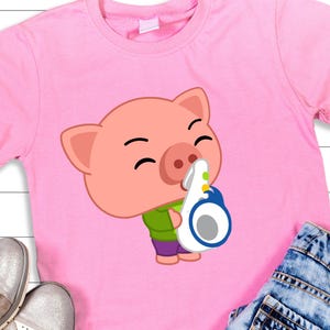 May include: Pink t-shirt featuring a cartoon pig wearing a green shirt and purple pants, holding a white and blue object. The pig has a smiling expression. The shirt is displayed with silver shoes and blue jeans.
