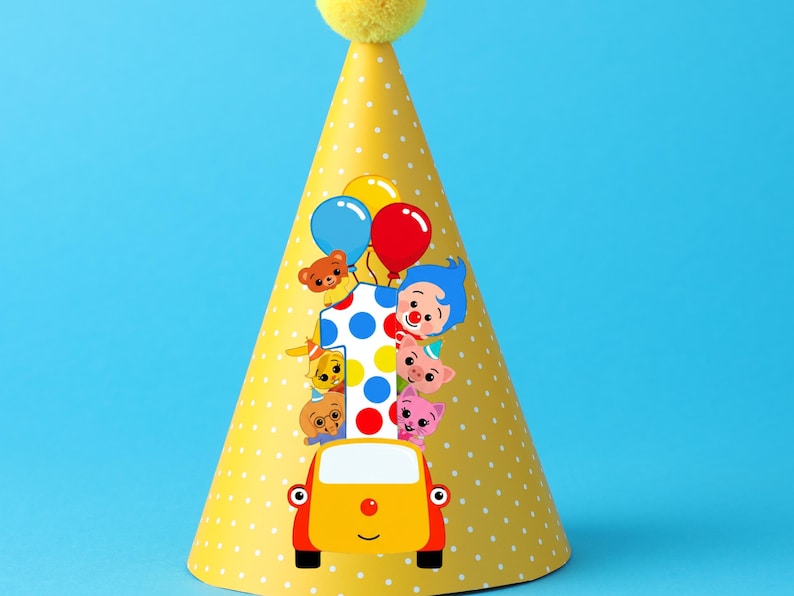 Op de afbeelding: Een gele feesthoed met witte stippen en een gele pompon. De hoed heeft een kleurrijke afbeelding van een auto met stripfiguren, ballonnen en het nummer 1. De achtergrond is effen blauw.