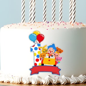 Op de afbeelding: Een witte verjaardagstaart versierd met een kleurrijk cartoonontwerp met het nummer 1, ballonnen en personages. De taart is bekroond met zes zwart-wit gestreepte kaarsen en hagelslag.