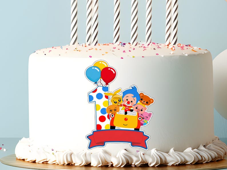 Op de afbeelding: Een witte verjaardagstaart versierd met een kleurrijk cartoonontwerp met het nummer 1, ballonnen en personages. De taart is bekroond met zes zwart-wit gestreepte kaarsen en hagelslag.