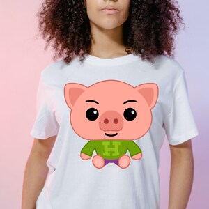 May include: White t-shirt featuring a cartoon pig design. The pig is pink with a green shirt and purple shorts. The letter "H" is on the shirt. The shirt is on a person.