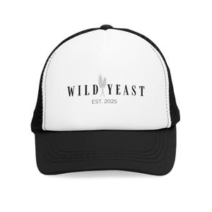 Puede incluir: Gorra de camionero en blanco y negro con el texto "WILD YEAST" y "EST. 2025" impreso en la parte delantera. La gorra tiene un panel frontal blanco con una visera negra y una parte trasera de malla. Un gráfico de trigo está entre las palabras.