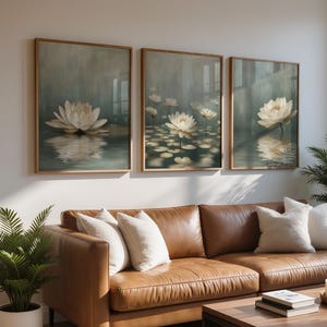 K&ouml;nnte beinhalten: Drei gerahmte Kunstdrucke mit wei&szlig;en Lotusblumen auf Wasser. Das Kunstwerk hat eine weiche, ged&auml;mpfte Farbpalette mit Fokus auf die Blumen und ihre Spiegelungen. Die Drucke werden &uuml;ber einem braunen Ledersofa ausgestellt.