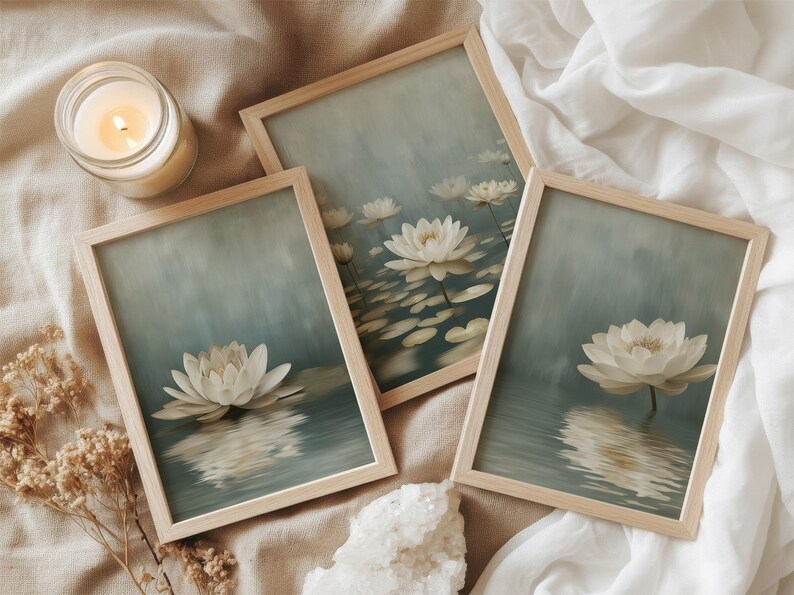 K&ouml;nnte beinhalten: Drei gerahmte Kunstdrucke mit wei&szlig;en Lotusbl&uuml;ten auf Wasser, in einem weichen blau-gr&uuml;nen Aquarellstil. Die Rahmen sind aus hellem Holz. Eine brennende Kerze und Trockenblumen sind ebenfalls vorhanden.