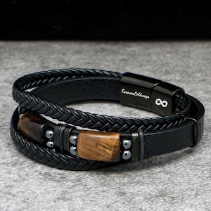 Puede incluir: Pulsera de cuero negro con diseño trenzado y detalles de madera. La pulsera tiene un cierre magnético con el texto "Forever Always" y un símbolo de infinito. La pulsera es de varias capas y tiene un estilo moderno y masculino.