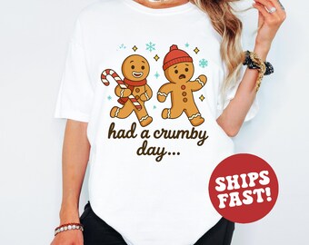 May include: White t-shirt with a design of two gingerbread men and the text "had a crumby day...". One gingerbread man has a candy cane and scarf, the other a red hat. The design includes snowflakes and stars, perfect for the festive season.