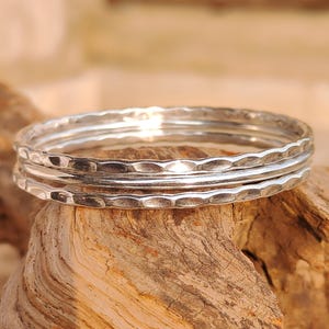 May include: A set of three silver-colored rings stacked together. The top and bottom rings feature a hammered, textured surface, while the middle ring has a smooth, polished finish. The rings are circular and metallic in appearance.