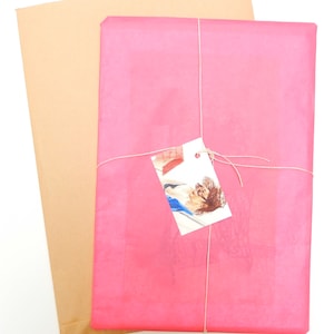May include: A pink tissue paper package tied with twine and a small white tag. The tag has a drawing of a person with a red book.