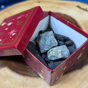 May include: A red gift box with gold stars printed on it is open, revealing a collection of dark gray and black stones inside.