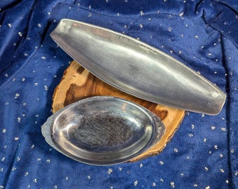 May include: Two silver metal serving dishes on a wooden base. The larger dish is oval shaped and the smaller dish is round.