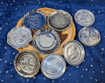 May include: Nine silver-toned metal coasters with various designs. The coasters feature floral, geometric, and animal motifs.