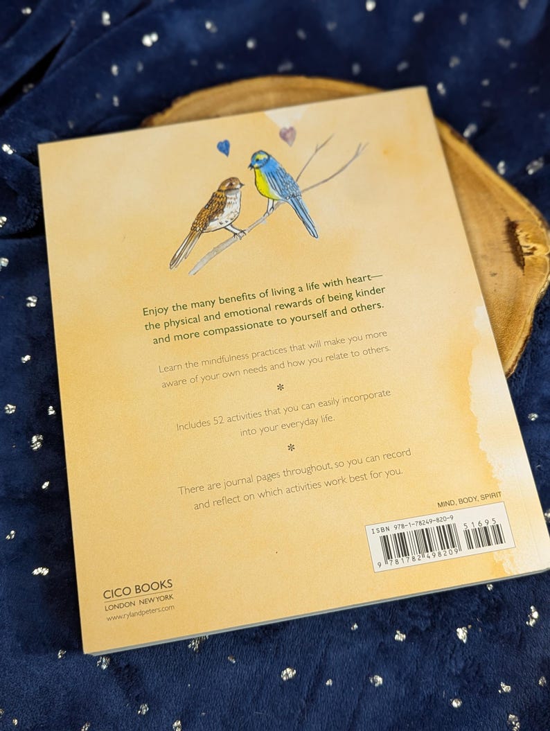 May include: A book cover with a watercolor illustration of two birds perched on a branch, with text about mindfulness and kindness. The book is titled "Mind, Body, Spirit" and includes 52 activities for everyday life.