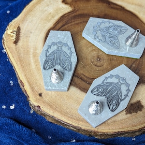 May include: Three gray hexagonal incense holders with a cone-shaped incense burner in the center of each. Each holder features a detailed etched design of a moth with wings spread.