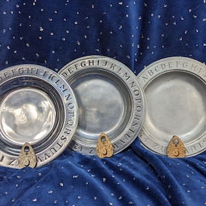 May include: Three circular metal plates featuring an embossed alphabet from A to Z and numbers 1 through 0 along the rim. Each plate is accompanied by a small, light-colored wooden planchette engraved with a crescent moon and the word GOODBYE.