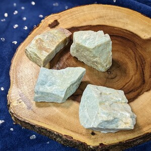 May include: Four rough-cut, light blue and white, green aventurine crystal stones on a wooden slice.