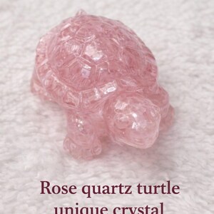 May include: A pink rose quartz turtle figurine. The turtle is carved with detailed shell and body features. The image includes the text "Rose quartz turtle unique crystal".