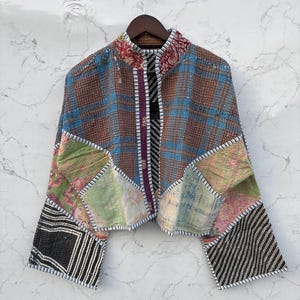 May include: A cropped jacket featuring a patchwork design of various fabrics including brown and blue plaid, floral patterns in green and pink, and black and white striped sections. The garment has a mandarin collar and white stitched edges.
