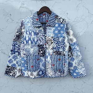 May include: A quilted jacket featuring a patchwork design of blue and white floral, striped, and botanical patterns. The garment includes a collared neckline, a button-front closure, and two front pockets adorned with small red heart accents.