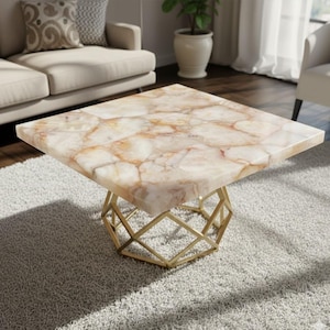 May include: Square coffee table with a cream and brown patterned top. The table has a gold geometric base and sits on a grey carpet. The table is a modern piece of furniture.