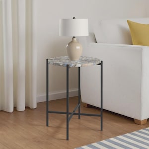 May include: A round side table with a black metal frame and a patterned stone top. A cream-coloured lamp with a white shade sits on the table. The table is approximately 61 cm tall.