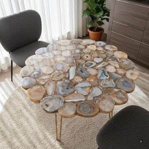 May include: A round coffee table with a mosaic top made of polished agate slices in shades of beige, grey, and blue. The table has gold-coloured metal legs. The table is approximately 91 cm in diameter.